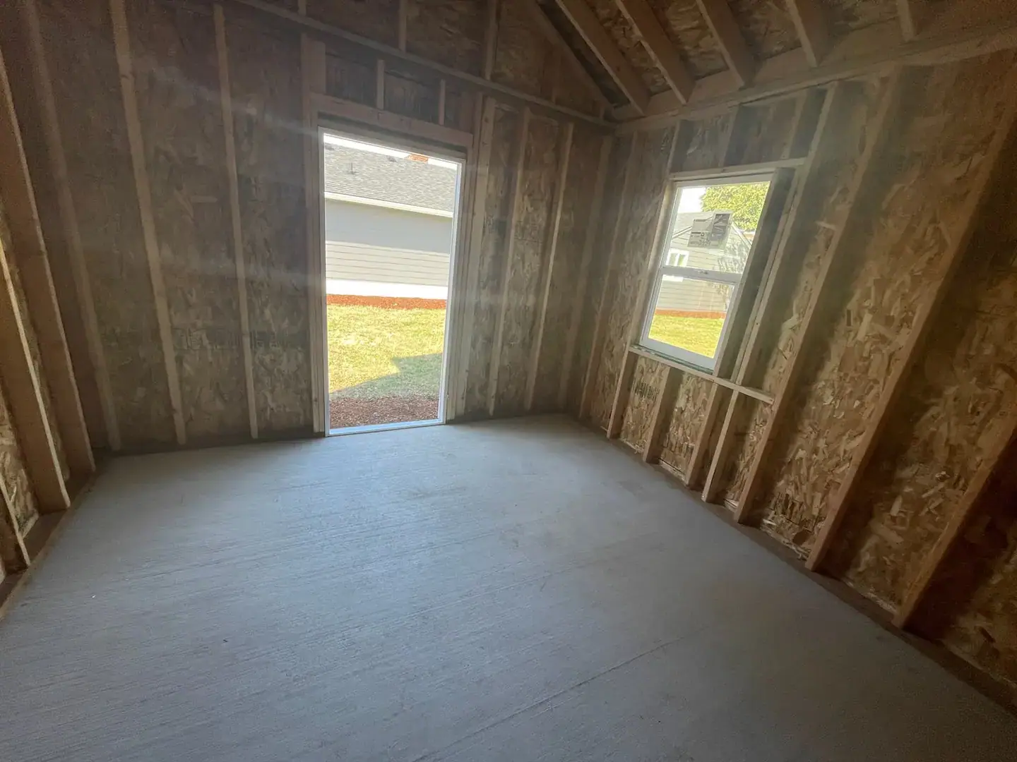 Framed interior of a new backyard building with door and window openings on a fresh concrete slab